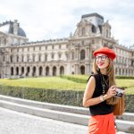 Young woman tourist in red cap walking with photo camera near the famous Louvre museum in Paris