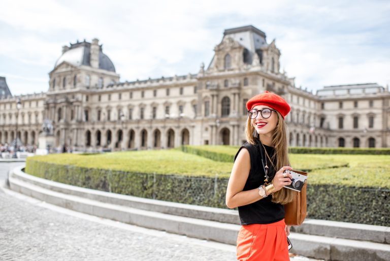 Young woman tourist in red cap walking with photo camera near the famous Louvre museum in Paris